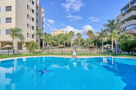 A swimming pool surrounded by palm trees and buildings.. '1 Dorm Delta' Apartment with Shared Pool, Wi-Fi & Air Conditioning
