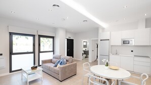 A modern living room with a sofa, a glass coffee table, and a dining area with a white table and chairs. - Apartment '2-Bed Antares' with Shared Pool, Wi-Fi, and Air Conditioning (Torre del Mar)