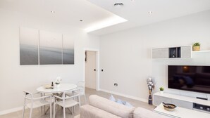 A modern living room with a sofa, dining table, chairs, a flat-screen TV, and artwork on the wall. - Apartment '2-Bed Antares' with Shared Pool, Wi-Fi, and Air Conditioning (Torre del Mar)