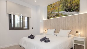 Un dormitorio moderno con una cama grande, dos mesitas de noche con lámparas, un ventanal con persianas y un cuadro colgado en la pared.