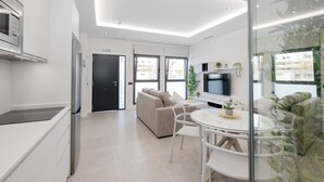 Una cocina moderna con horno empotrado, comedor con mesa y sillas de vidrio, sofá y televisor fijado a la pared.