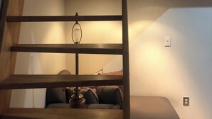 Una camera da letto in stile loft con una scala in legno che porta a un letto a castello. In primo piano, un tavolino con una lampada.