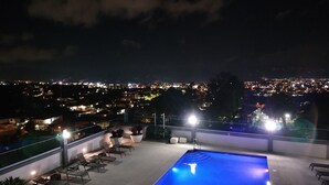 Ein Pool auf dem Dach mit Liegestühlen und Blick auf eine nächtliche Stadtlandschaft.