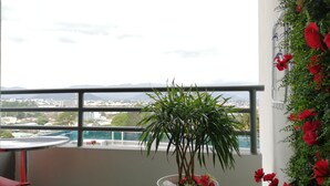 Ein Balkon mit einem Blumentopf, einem roten Stuhl und Blick auf eine Stadtlandschaft.