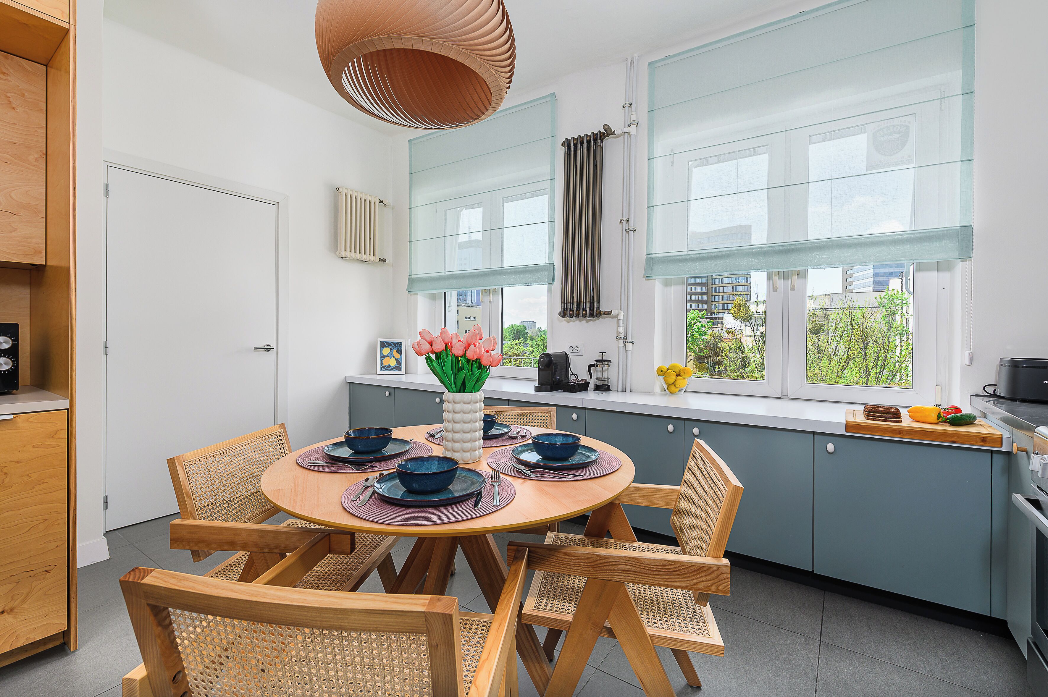 Eine moderne Küche mit einem runden Esstisch, Holzstühlen und Blick auf die Stadt durch große Fenster.