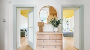 Une pièce avec une commode en bois, un miroir et une plante en pot. Deux portes donnent accès à d’autres pièces.