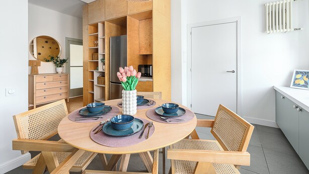 Un espace repas moderne avec une table ronde en bois, de la vaisselle bleue et des chaises en osier.