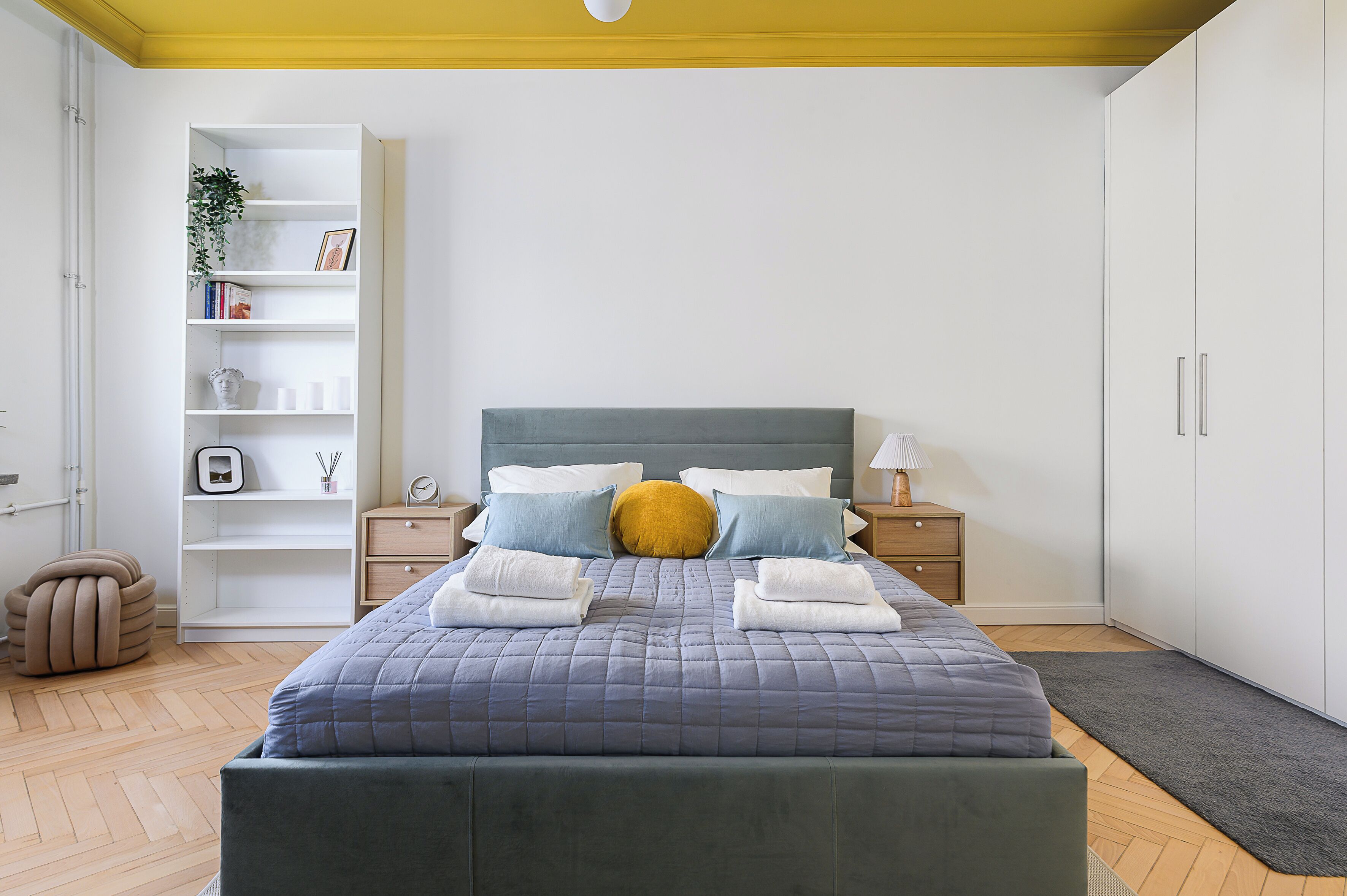 A neatly arranged bedroom with a bed, bedside tables, a wardrobe, and a built-in shelving unit.