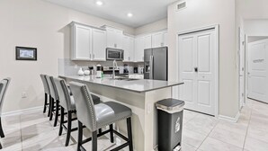 A modern kitchen with white cabinets, a stainless steel refrigerator, and a central island with bar stools.