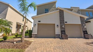 A modern two-story house with a garage, numbered 1153 and 1155, surrounded by a landscaped driveway and small trees.