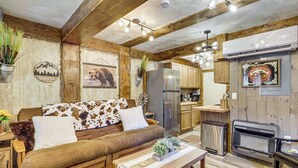 A rustic cabin interior with a wooden sofa, a dining table, a kitchen area, and a fireplace. - Eureka Main Street Retreat Near ATV Trails & Mines (Eureka)
