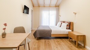 Ein Schlafzimmer mit Bett, Nachttisch, Sessel und Schreibtisch mit Blumenvase.
