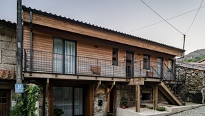 Ein zweistöckiges Gebäude mit Holzfassade, einem Balkon mit Metallgeländer und einer Steintreppe, die zu einer oberen Ebene führt.