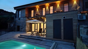 Ein zweistöckiges Haus mit Schwimmbad, Sitzgelegenheiten im Freien und einer überdachten Terrasse.