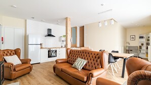 Ein modernes Wohnzimmer mit einem braunen Ledersofa, einem Esstisch und einer Küche im Hintergrund.