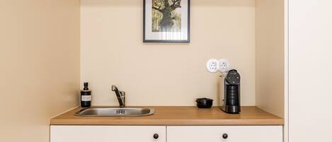A kitchen with a sink, a coffee maker, a small pot, and a framed picture on the wall.
