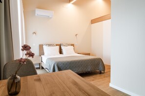 Een slaapkamer met een bed, nachtkastje, stoel en een vaas met bloemen.