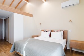 Une chambre à coucher comprenant un lit, une tête de lit en bois, des tables de chevet, un appareil de climatisation et une porte donnant sur une autre pièce.