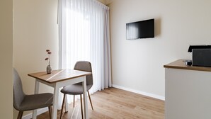 A modern room with a wooden dining table, two chairs, a TV mounted on the wall, and a small kitchenette area.