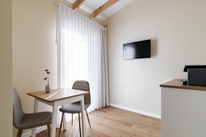 Une pièce moderne avec une table à manger en bois, deux chaises, un téléviseur fixé au mur et un petit coin cuisine.