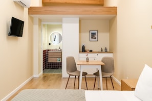 A compact hotel room with a bed, a small desk, two chairs, a TV, a mirror, a picture on the wall, and a bathroom with a sink and mirror. - 'Avó Custódia - Room' with Mountain View, Wi-Fi and Air Conditioning (Terras de Bouro)
