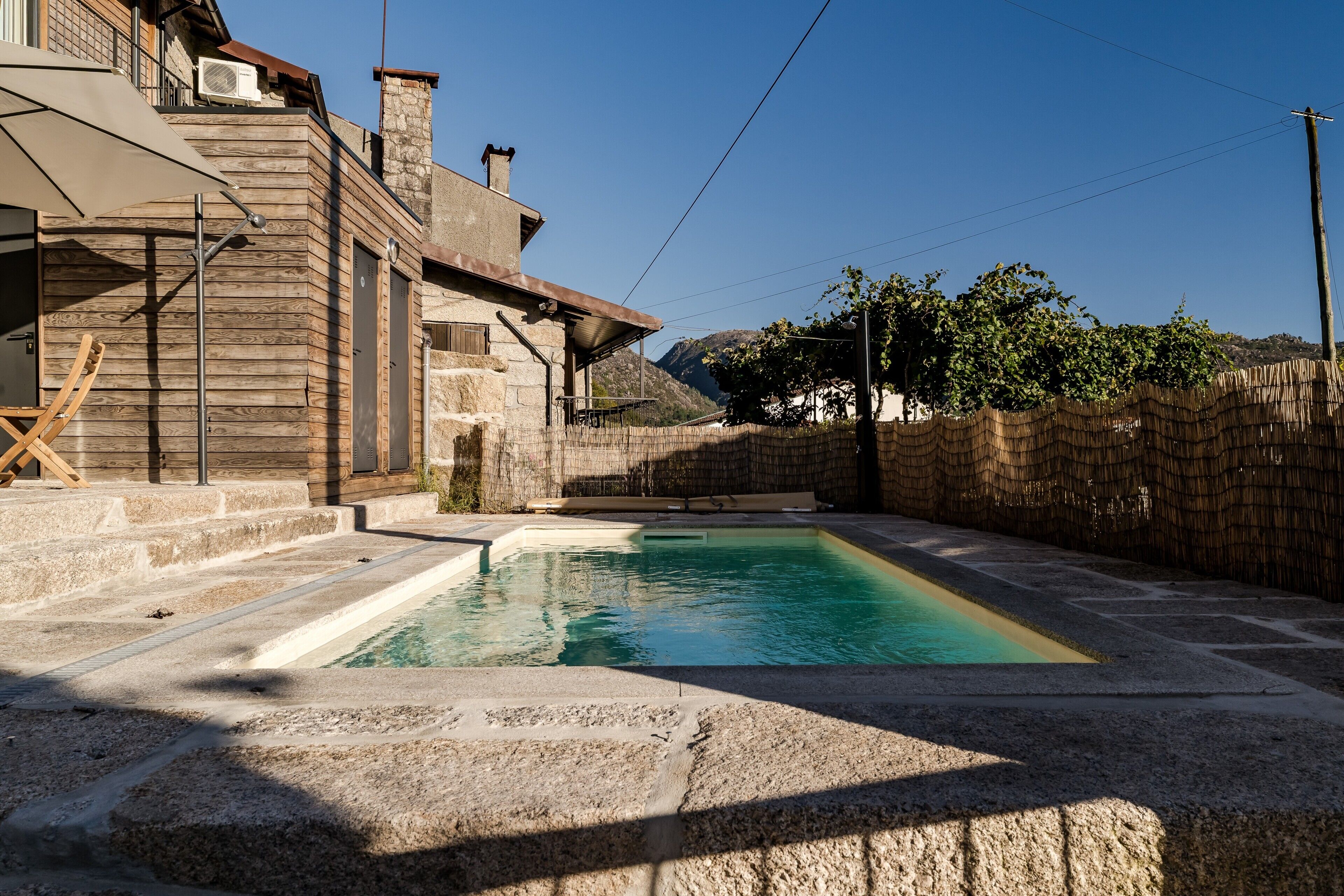 A pool area with a stone deck, a wooden building with a balcony, and a stone wall.