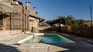 A pool area with a stone deck, a wooden building with a balcony, and a stone wall.