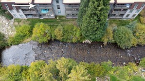Eine Vogelperspektive auf ein modernes, mehrgeschossiges Gebäude mit Balkonen, einem Fluss davor und umliegender Bepflanzung.