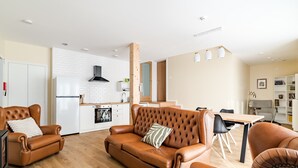 Un salon moderne avec un canapé en cuir marron, une table à manger et un coin cuisine en arrière-plan.