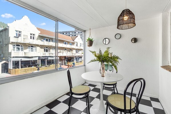 A room with a checkered floor, a round table with two chairs, a potted plant, and a hanging light fixture.