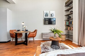 A dining area with a table, chairs, a vase with flowers, a bookshelf, and a flat-screen TV mounted on the wall.