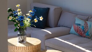 Ett modernt vardagsrum med en beige soffa, en vas med blommor och ett inramat konstverk med ett lövmotiv på väggen.