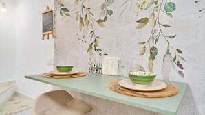 A dining area with a green table, two bowls, a white vase, and a wall with a leaf pattern. - Holiday Home 'Casa El Camaleón' with Wi-Fi and Air Conditioning (Almuñecar)