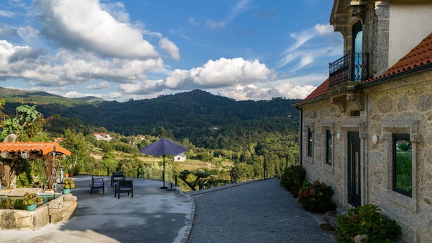 Ein Gebäude aus Stein mit rotem Ziegeldach, einem Balkon und Blick auf eine gebirgige Landschaft.