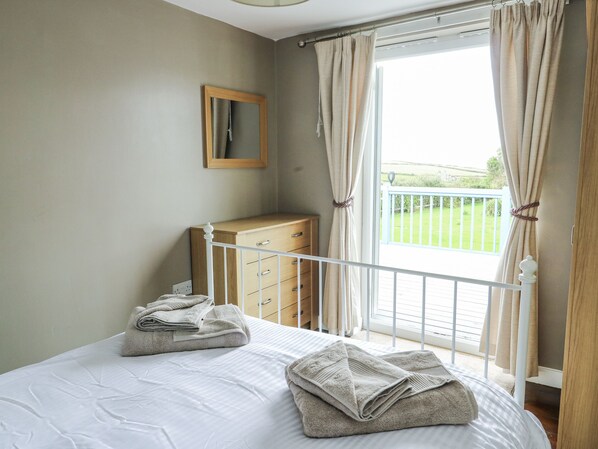 Une chambre à coucher avec un lit, une commode en bois, un miroir et un balcon avec des rideaux.