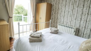 A bedroom with a bed, a wooden wardrobe, and a view of the outdoors. - Harbour Lights (Holyhead)