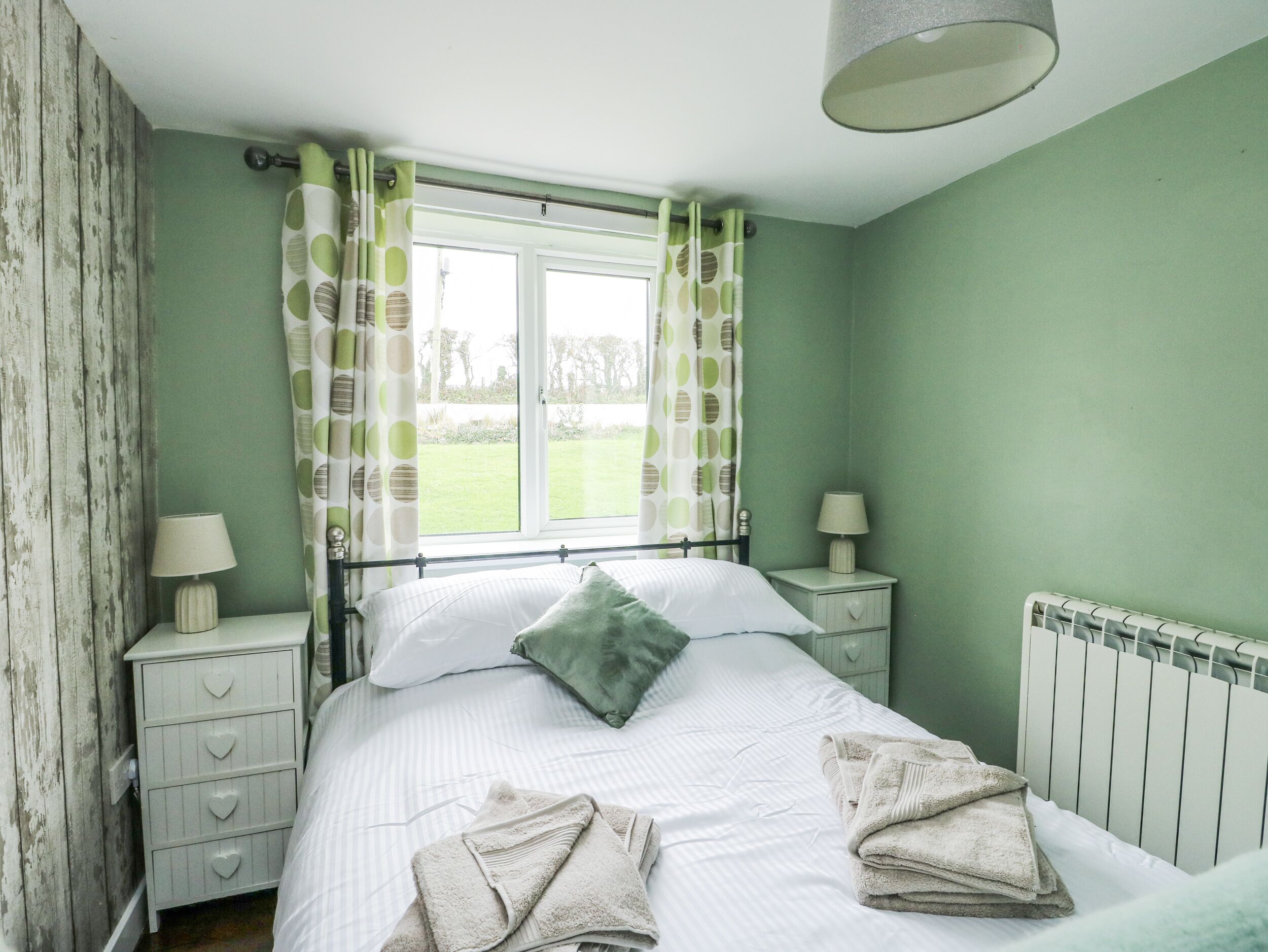A bedroom with a bed, two bedside tables, a window with curtains, and a radiator.