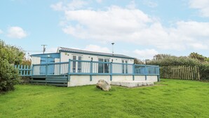 A single-story house with a blue exterior and white trim, surrounded by a green lawn and a wooden fence. - Harbour Lights (Holyhead)