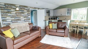 A cozy living room with two brown leather sofas, a white rug, and a kitchen in the background. - Harbour Lights (Holyhead)