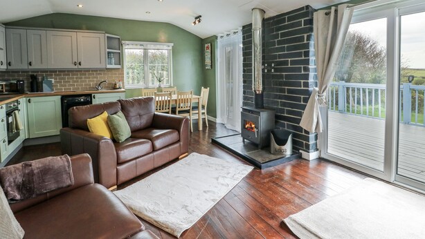 A cozy living area with a fireplace, a dining table, and a kitchen in the background. - Harbour Lights (Holyhead)