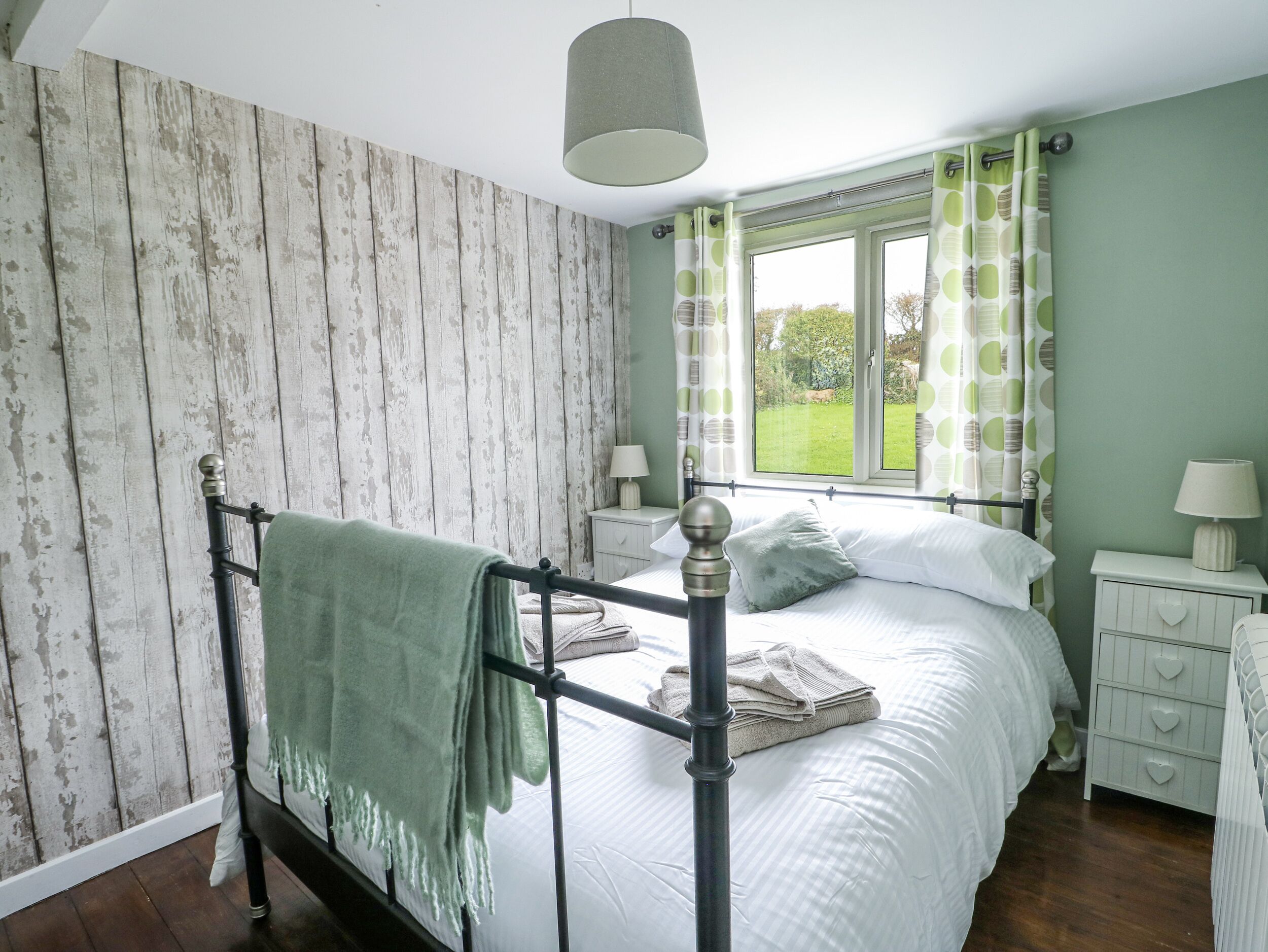 A bedroom with a four-poster bed, a window with curtains, a bedside table with a lamp, and a nightstand with a lamp.