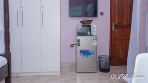A room with a bed, a wardrobe, a small refrigerator, a microwave, and a television on the wall.