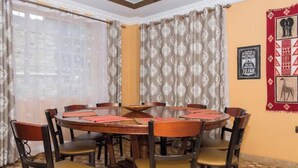 A dining area with a round wooden table surrounded by chairs, a window with curtains, and a wall with framed pictures.