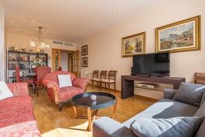 A living room with a sofa, armchair, TV, bookshelf, and paintings.