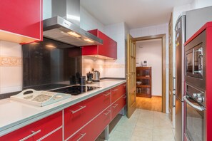A kitchen with red cabinets, a stainless steel range hood, a glass cooktop, and a refrigerator.