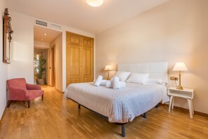 A bedroom with a bed, bedside lamps, a chair, and wooden flooring.