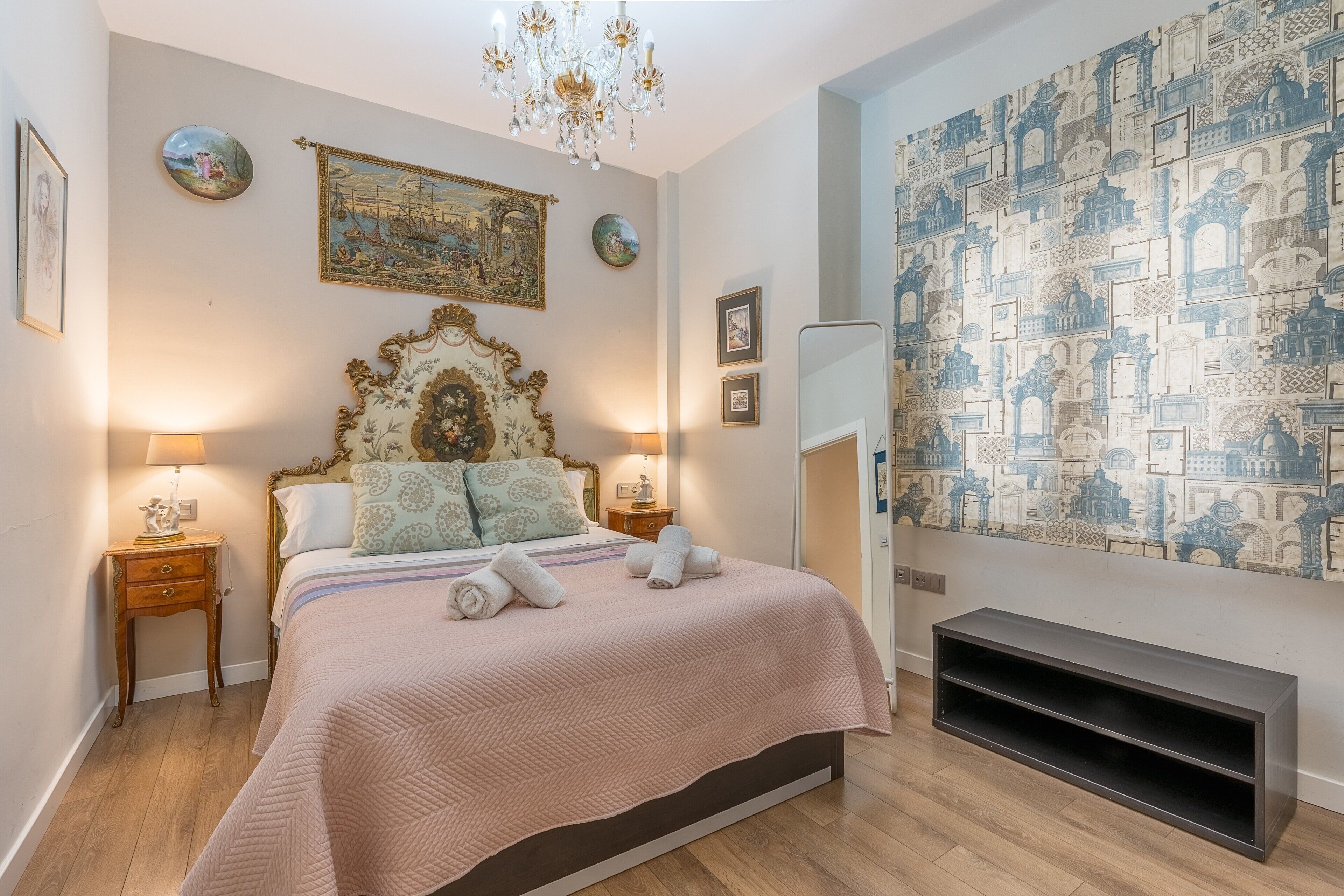 A bedroom with a bed, a chandelier, a wall tapestry, and a fireplace.