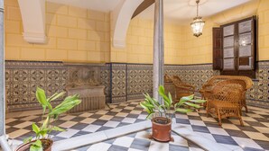 Un sol à carreaux, des plantes en pot, des chaises en osier et un mur orné de motifs.