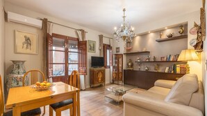 Un salon comprenant un canapé, une table à manger avec des chaises, un téléviseur et des objets décoratifs disposés sur des étagères.