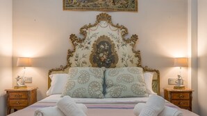 Un lit avec une tête de lit à motifs floraux, deux tables de chevet avec des lampes et deux serviettes enroulées posées sur le lit.